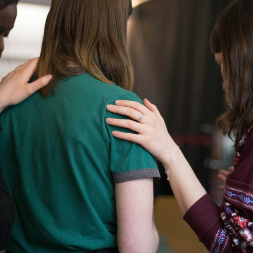 Support workers offering comfort and reassurance to a woman, with hands placed gently on her shoulders in a supportive group setting.